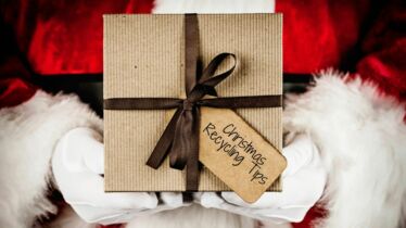 Santa holding a gift with a tag saying 'Christmas Recycling'