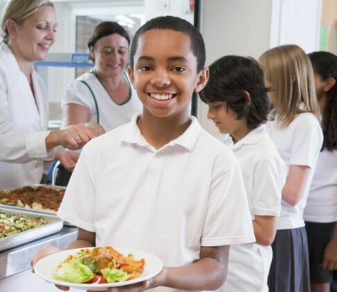 Queue in school canteen with children holding plates of food