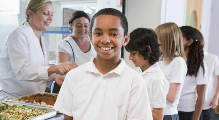 Queue in school canteen with children holding plates of food